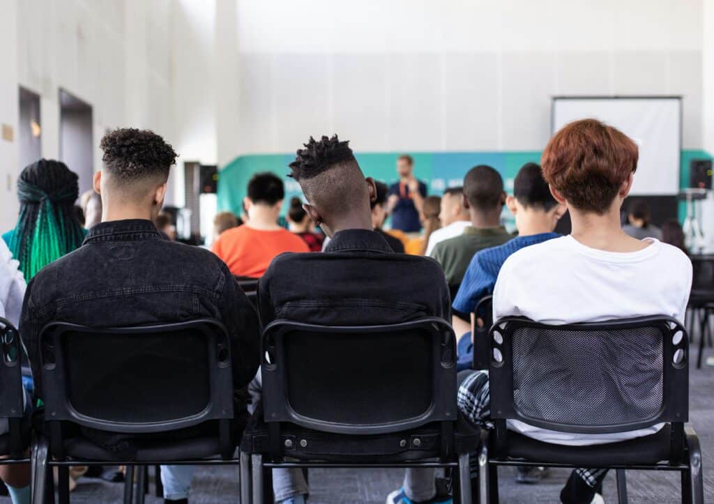 Estudantes assistindo a uma palestra ou aula em sala de aula moderna e bem iluminada, focados em intercâmbio cultural e educação internacional.